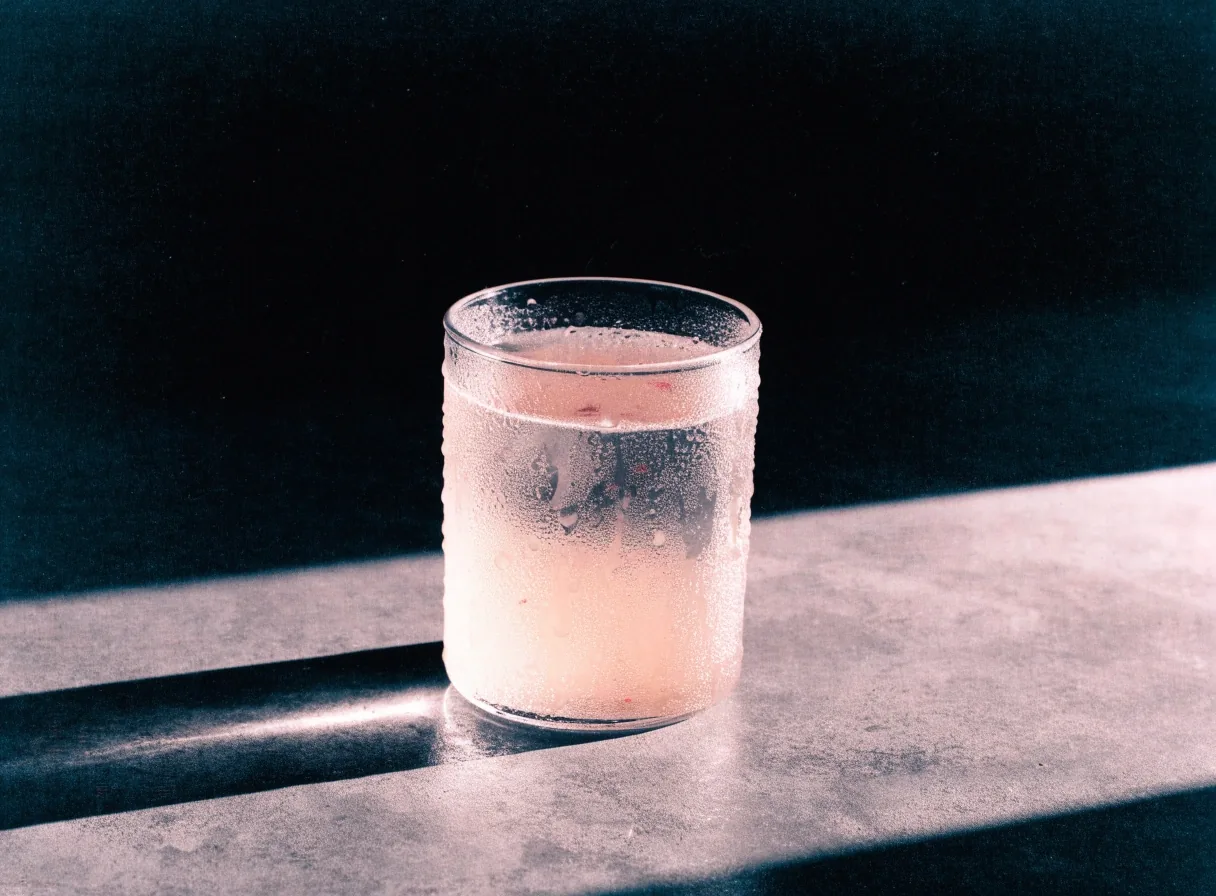 A condensation-covered cup of strawberry lemonade on a bare surface