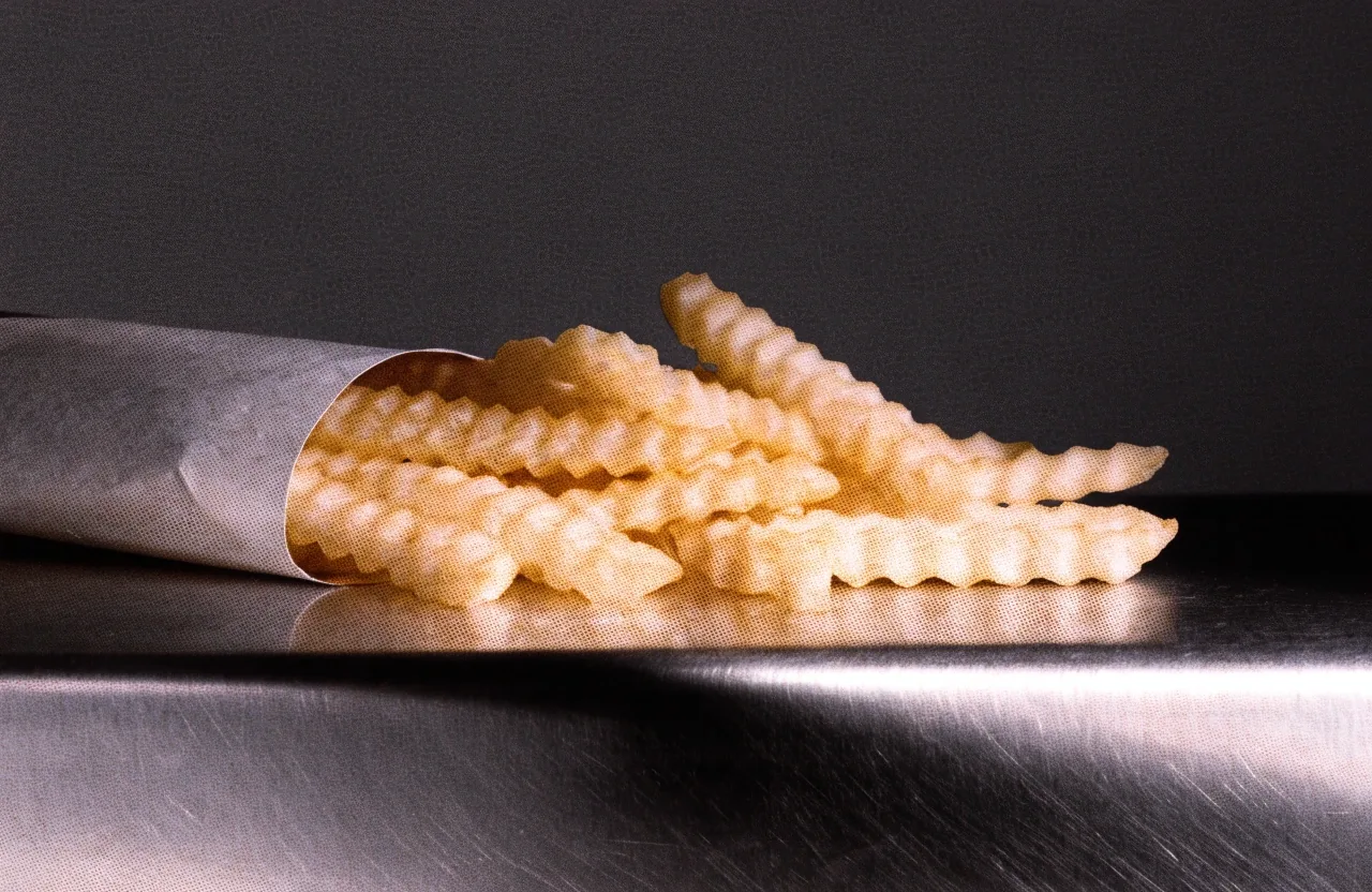 A handful of crinkle-cut fries held loose in a hand under hard raking light